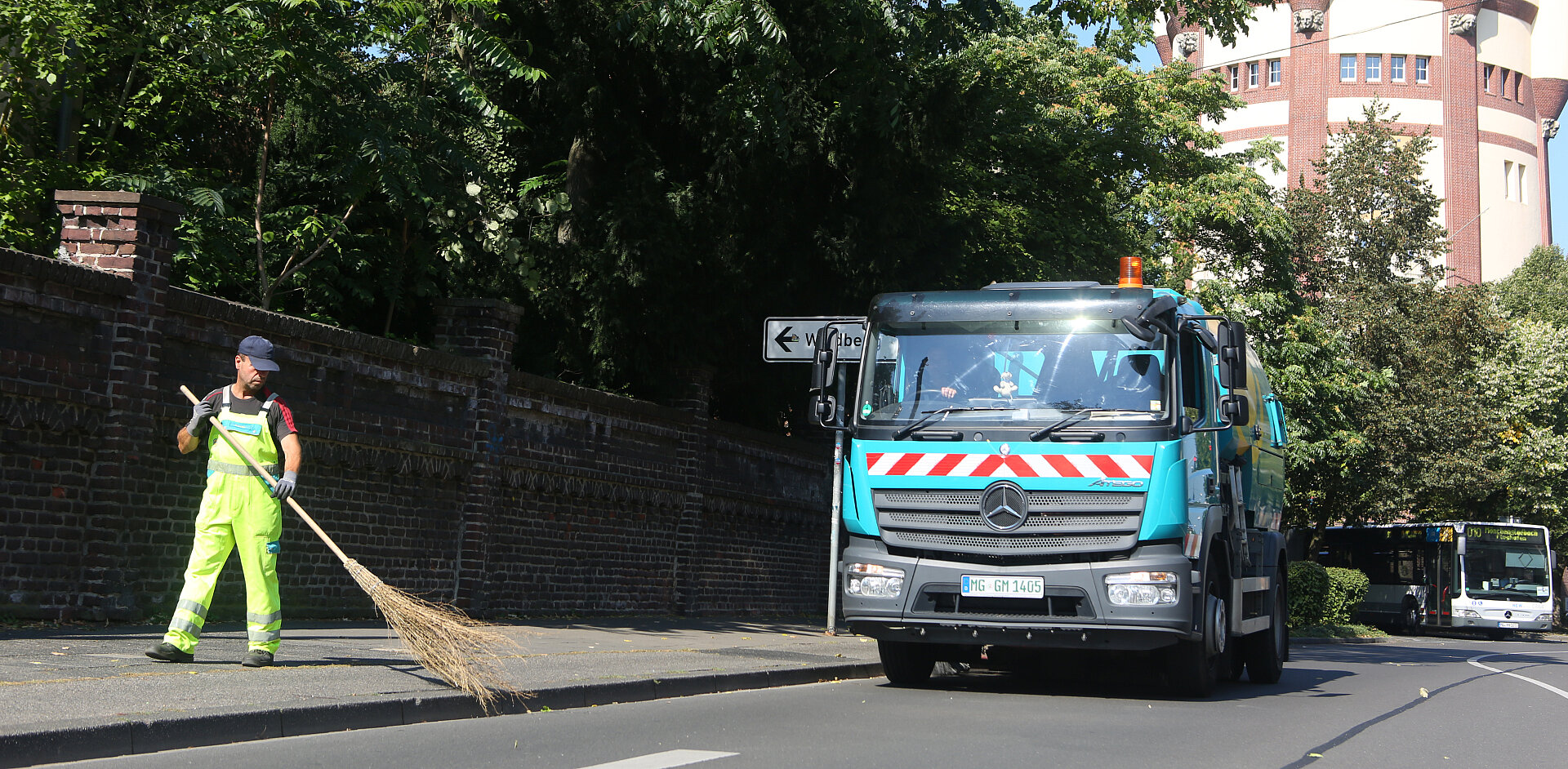 Die GEM ist für Straßenreinigung in Mönchengladbach verantwortlich wie hier am Wasserturm. Straßenreiniger der GEM fegt großer Kehrmaschine Schmutz zum Aufkehren zu.