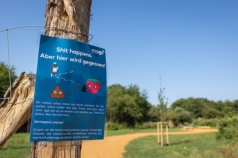 Eingang essbarer Waldgarten mit Infoschild an Hundehaltende